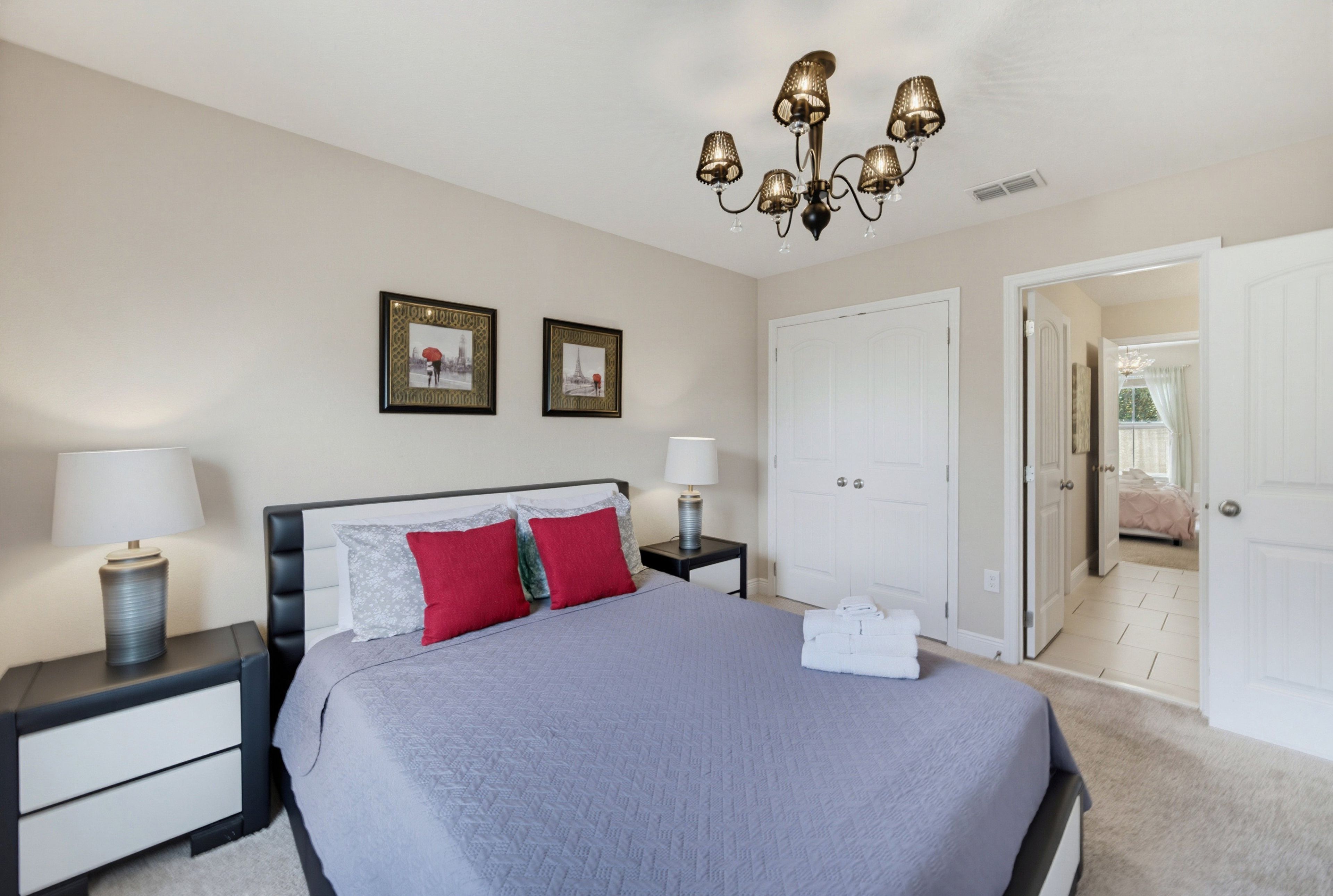 A bedroom with a large bed, two bedside tables with lamps, a chandelier, and two framed pictures on the wall.