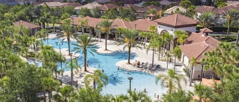 A resort with a central swimming pool, palm trees, and a view of surrounding houses.