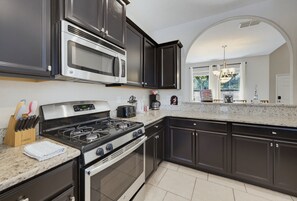 A modern kitchen with dark cabinetry, stainless steel appliances, and a granite countertop. - Luxury Solterra Resort Retreat | Near Disney (Davenport)
