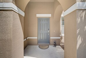 A building entrance with a grey door, a small porch area, and a dog standing by the door. - Luxury Solterra Resort Retreat | Near Disney (Davenport)