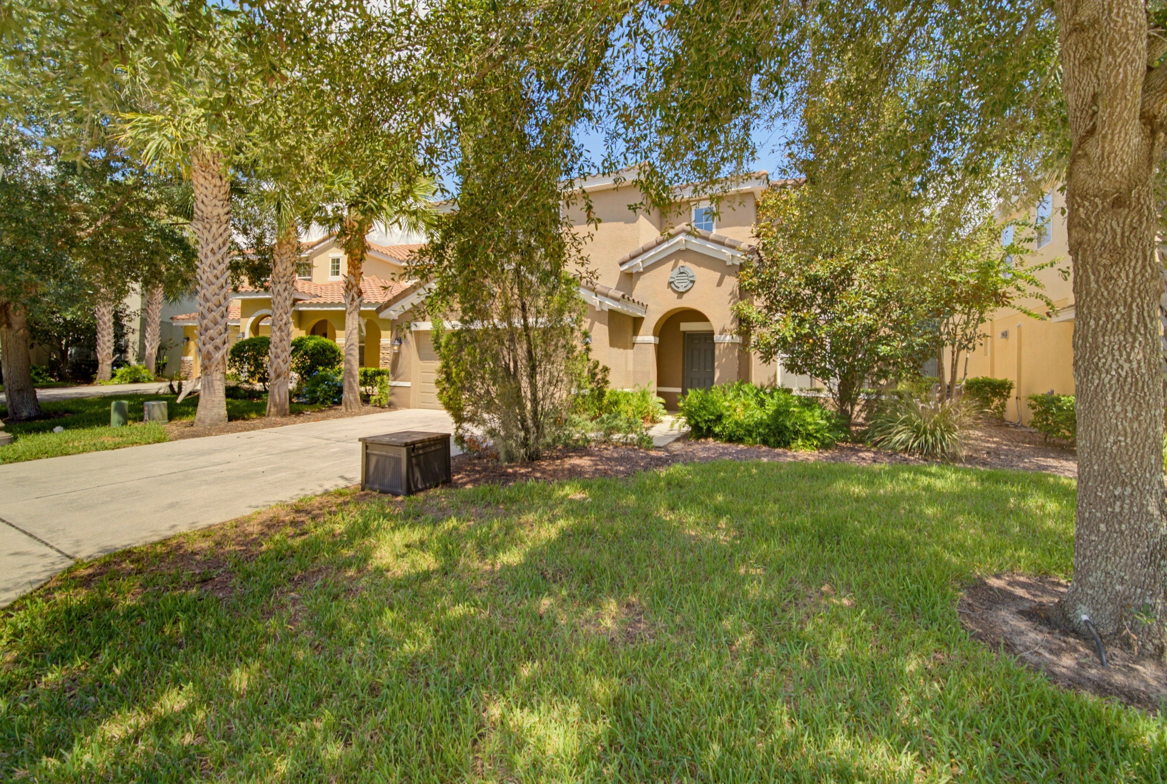 A residential area with a paved driveway, a lawn, and a building with a tiled roof and arched entrance.
