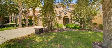 A residential area with a paved driveway, a lawn, and a building with a tiled roof and arched entrance.