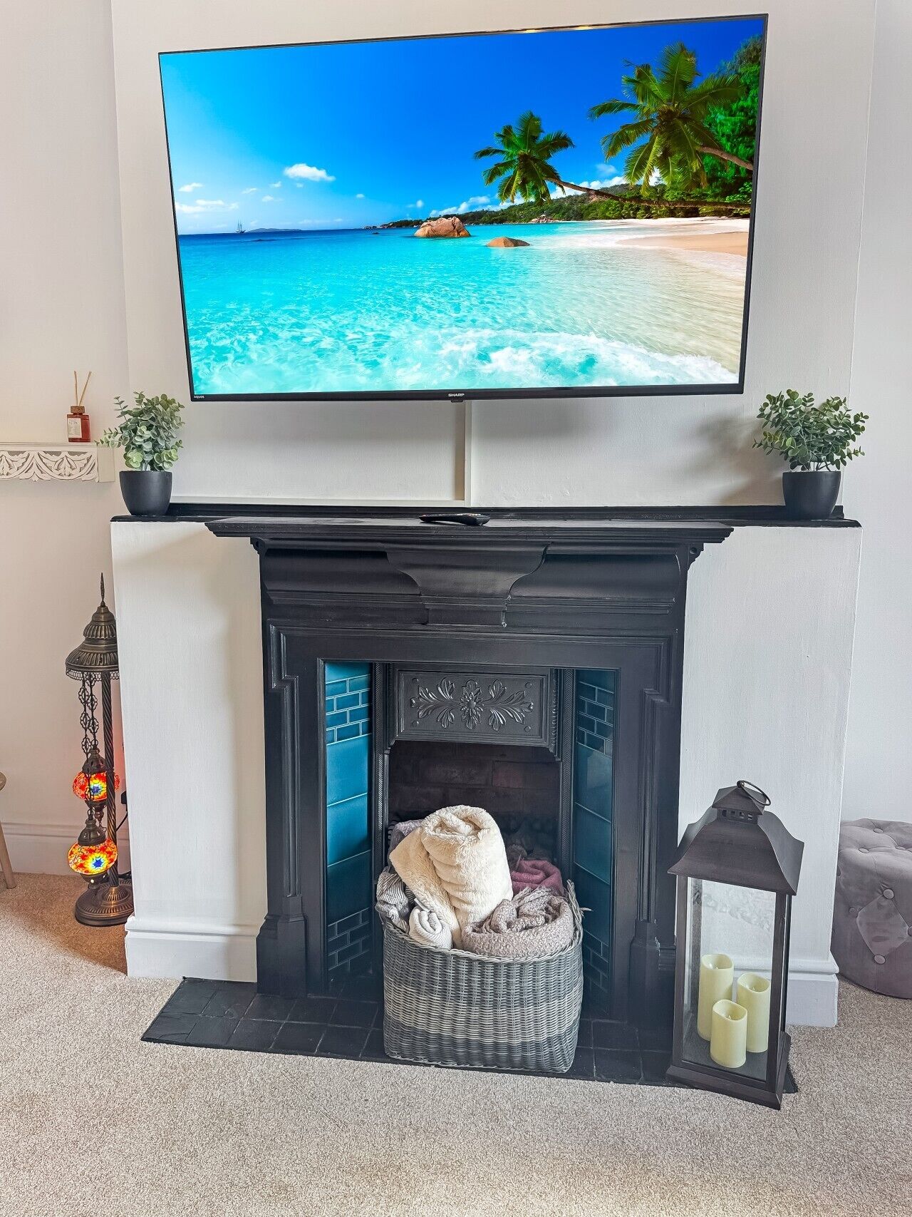 Un téléviseur à écran plat fixé au-dessus d’une cheminée, et l’écran affiche une scène de plage.