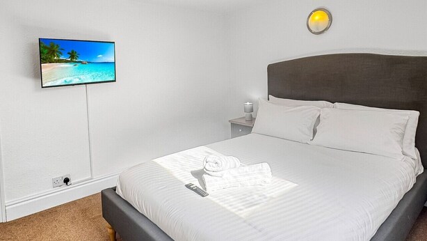 A bedroom with a bed, a TV mounted on the wall, a bedside table with a lamp, and a carpeted floor. - Sleeps 10 3 Bed Central Grantham with Parking (Grantham)
