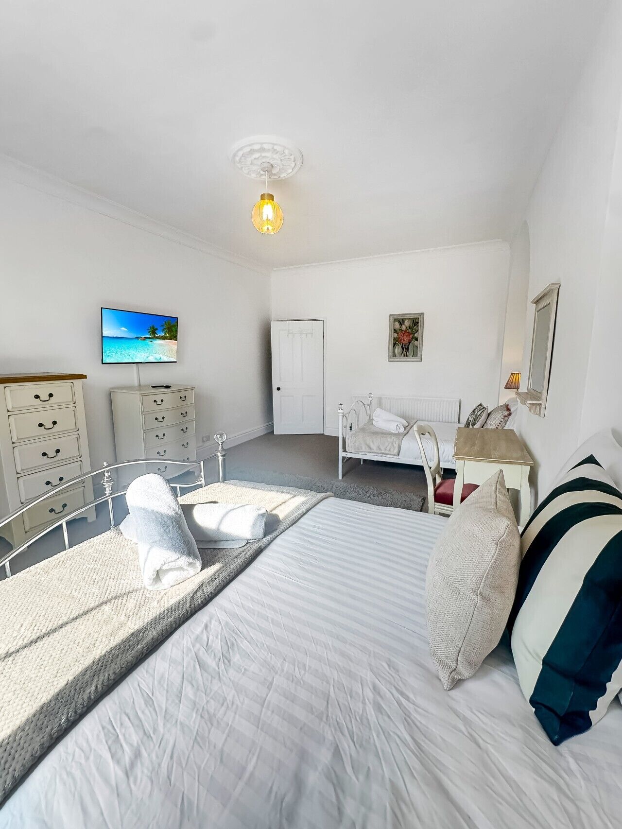 A bedroom with a bed, bedside tables, a dresser, a television, and a ceiling light.