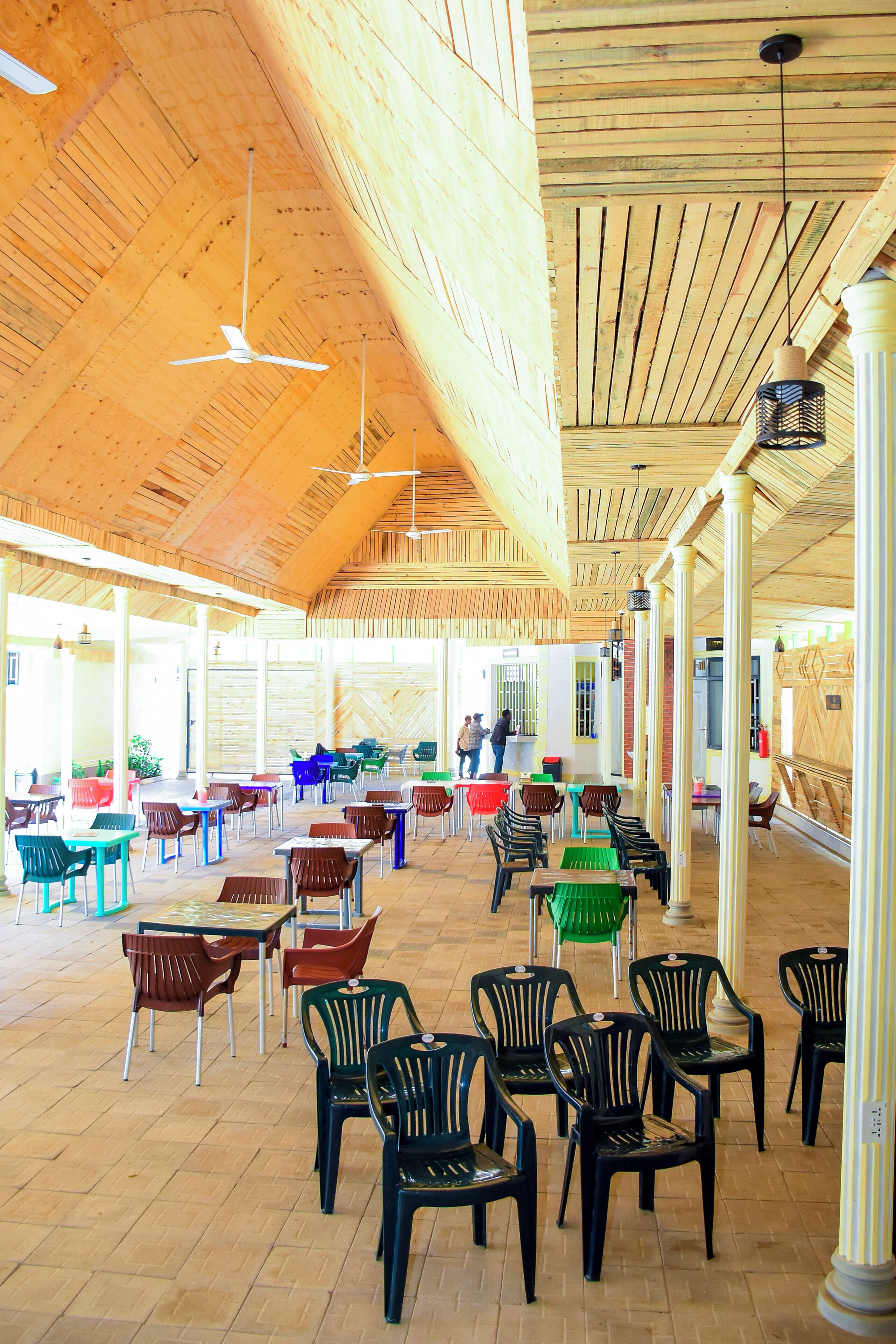 Un comedor interior con vigas de madera en el techo, varias mesas y sillas, y lámparas colgantes.