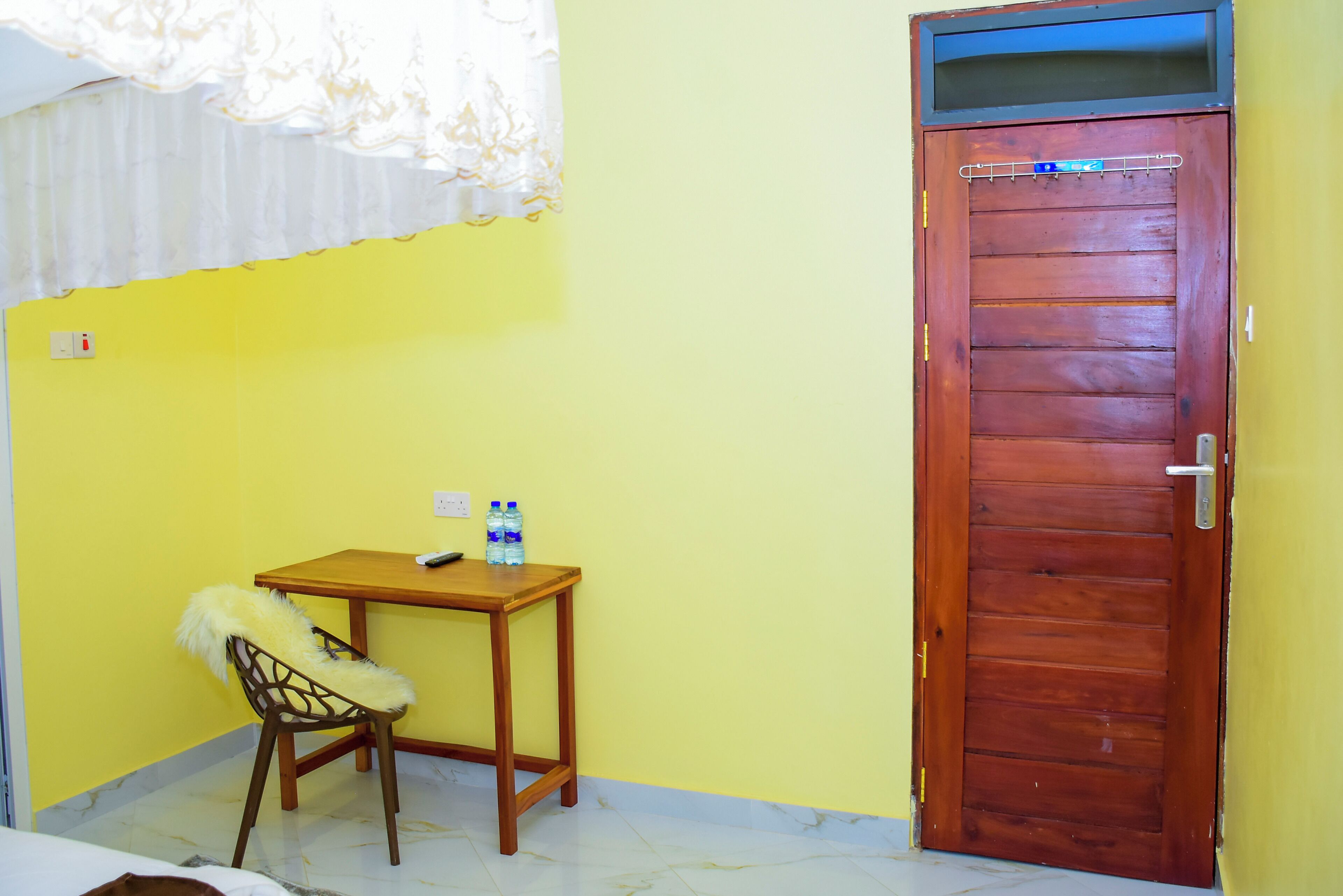 Um quarto com porta de madeira, uma mesa pequena com uma cadeira e duas garrafas de água sobre a mesa.