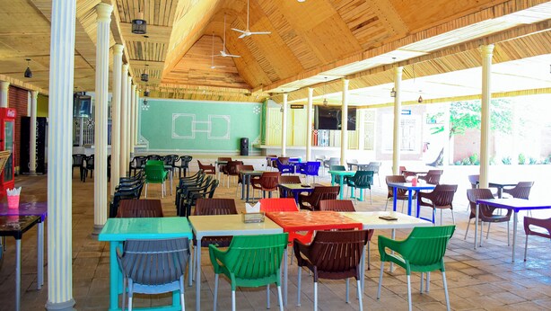 Un'area pranzo all'aperto coperta, con tavoli, sedie, una lavagna e un bancone.