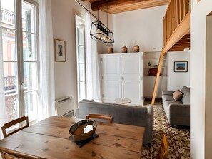A room with a wooden dining table, a grey sofa, a staircase, and a white cabinet. - Apartment 'A Stone's Throw From The Arènes' with Wi-Fi and Air Conditioning (Nîmes)