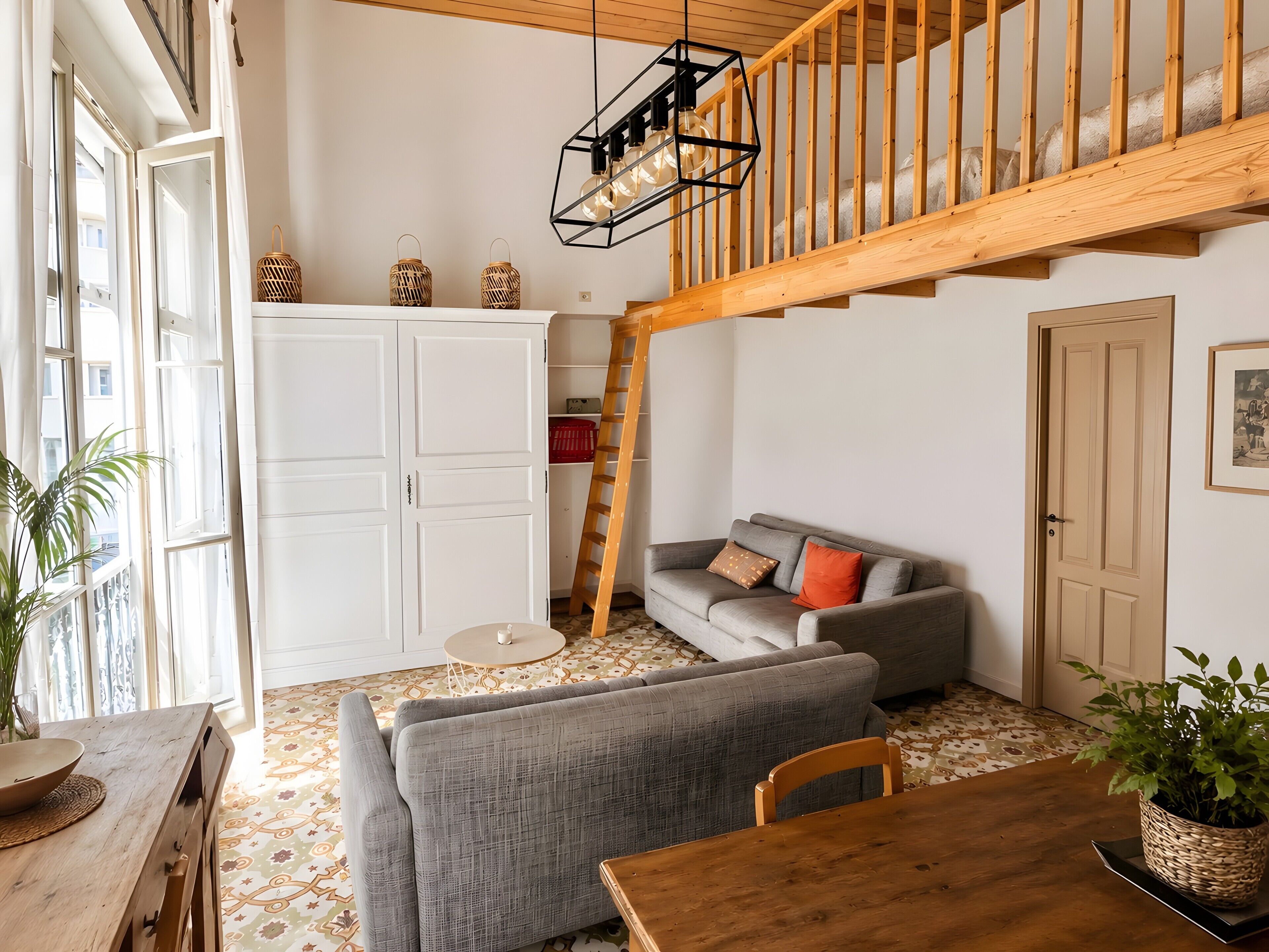 A room with a loft area, a grey sofa, a wooden dining table, and a staircase.