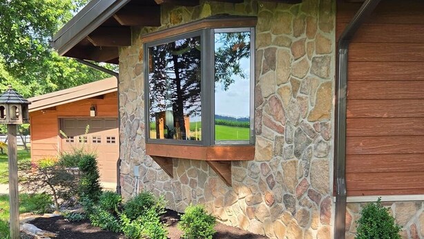 Ein Steinhäuschen mit Garage, ein Fenster spiegelt einen Baum wider, und ein Garten mit verschiedenen Pflanzen.