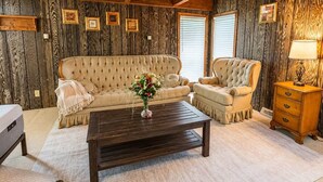 Ein Zimmer mit einer раnten Sofа, einem passenden Sessel, einem Holztisch und einem Nachttisch aus Holz.
