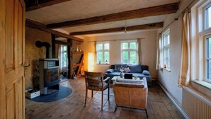 Ein rustikaler Raum mit freiliegenden Holzbalken, Kamin, einer Couch und einem Sessel.