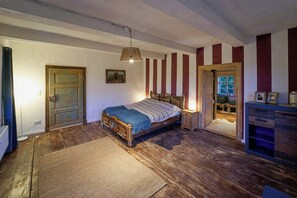 Ein Zimmer mit einem hölzernen Bett, einem kleinen Nachttisch, einem Teppich, einer Tür und einer Wand mit vertikalen Streifen.