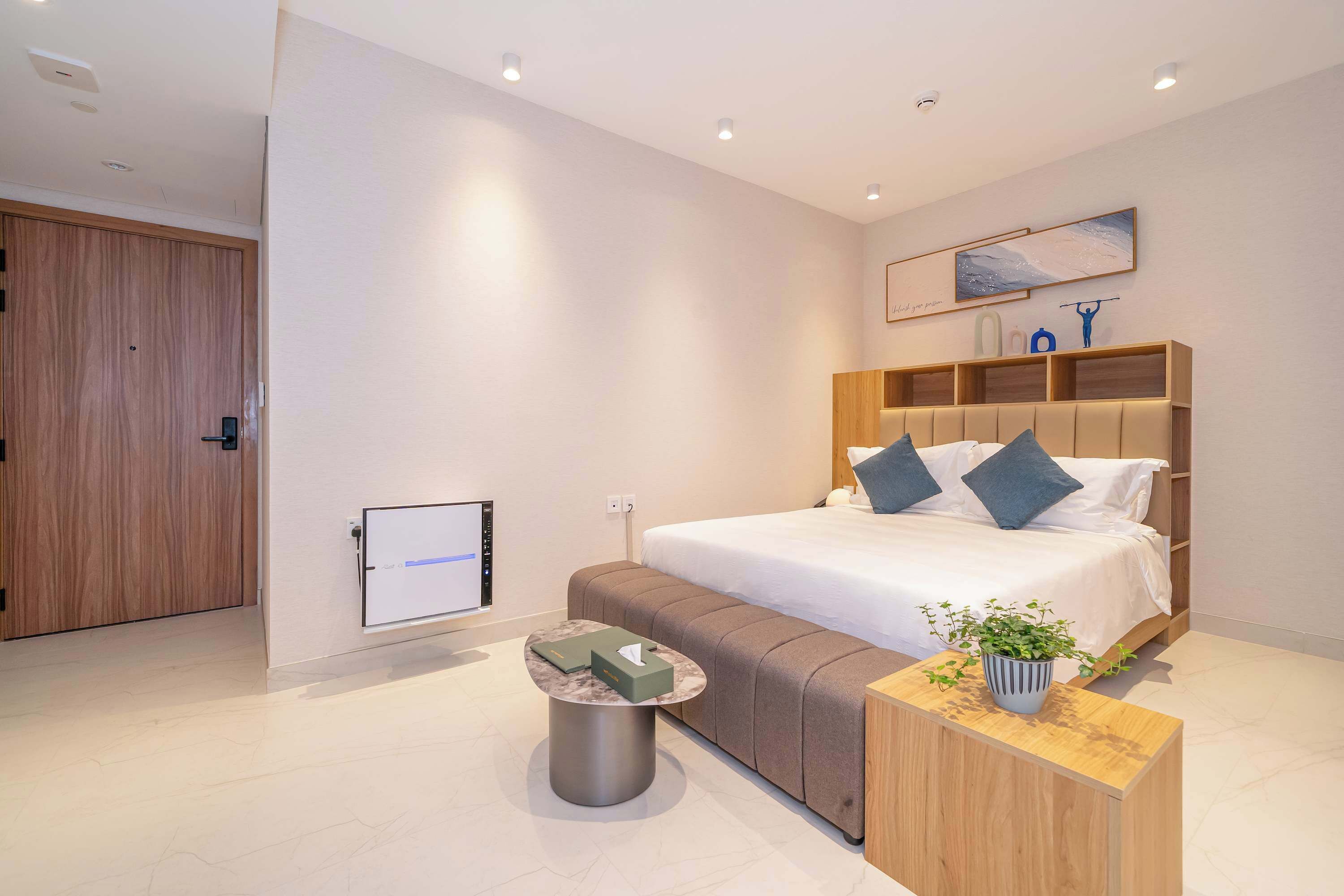 Een moderne slaapkamer met een groot bed, een nachtkastje, een klein rond tafeltje en een aan de muur bevestigde televisie.