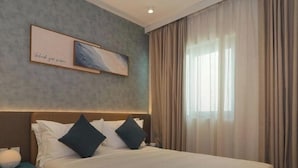 Ein Hotelzimmer mit einem Bett, einem Nachttisch, einem Wandbild und einem Fenster mit Vorhängen.