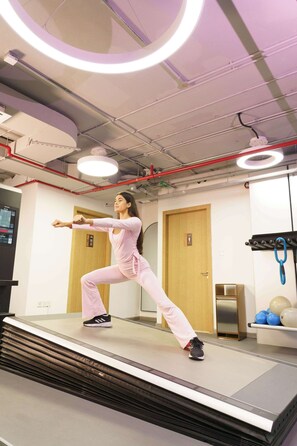 A person performing a stretching exercise on a platform with a digital display and a door in the background. - Executive Wellness Suite | Sauna, Pool & Gym (Jumeirah Village Triangle)