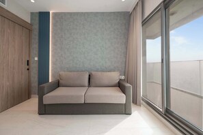 A modern living room with a sofa, a wooden wardrobe, and a large window. - Tranquil Deluxe Stay with Pool, Gym & Wellness (Jumeirah Village Triangle)