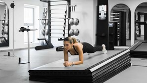 Ein Fitnessraum mit Trainingsgeräten, einer Person im Plank und einer Spiegelwand.