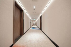 A hotel corridor with a carpeted floor, doors on both sides, and a patterned carpet runner in the center. - Tranquil Deluxe Stay with Pool, Gym & Wellness (Jumeirah Village Triangle)