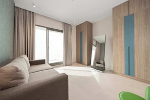 A modern hotel room with a sofa, a flat-screen TV, and a large window. - Tranquil Deluxe Stay with Pool, Gym & Wellness (Jumeirah Village Triangle)