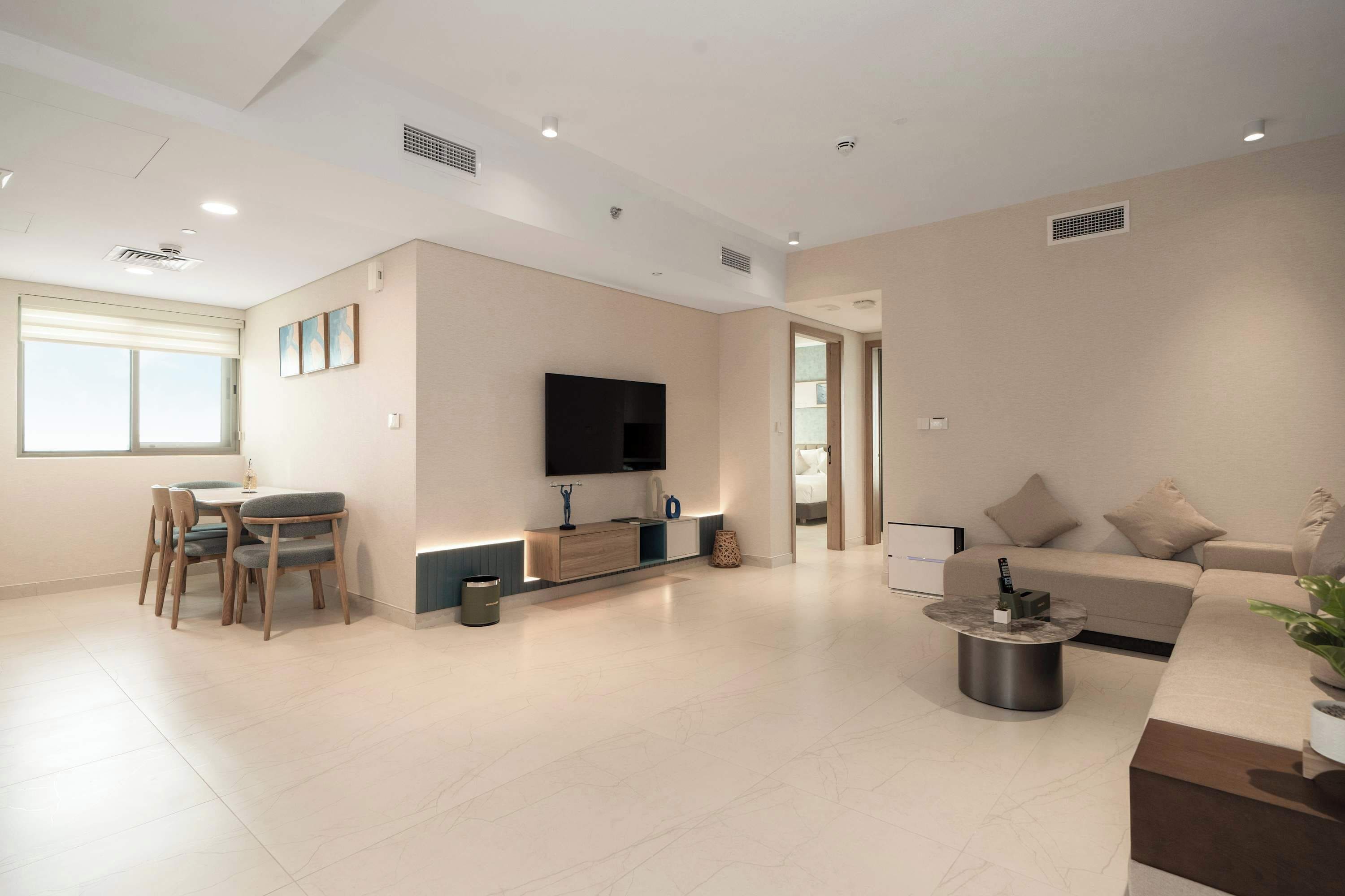 A modern living room with a flat-screen TV, a dining area with a table and chairs, and a sofa with a coffee table.