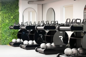 A row of exercise equipment with black handles and silver weights, set against a wall with a green leafy backdrop. - Tranquil Deluxe Stay with Pool, Gym & Wellness (Jumeirah Village Triangle)