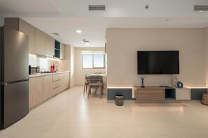A modern kitchen with built-in appliances, a dining area with a table and chairs, and a flat-screen TV mounted on the wall. - Tranquil Deluxe Stay with Pool, Gym & Wellness (Jumeirah Village Triangle)
