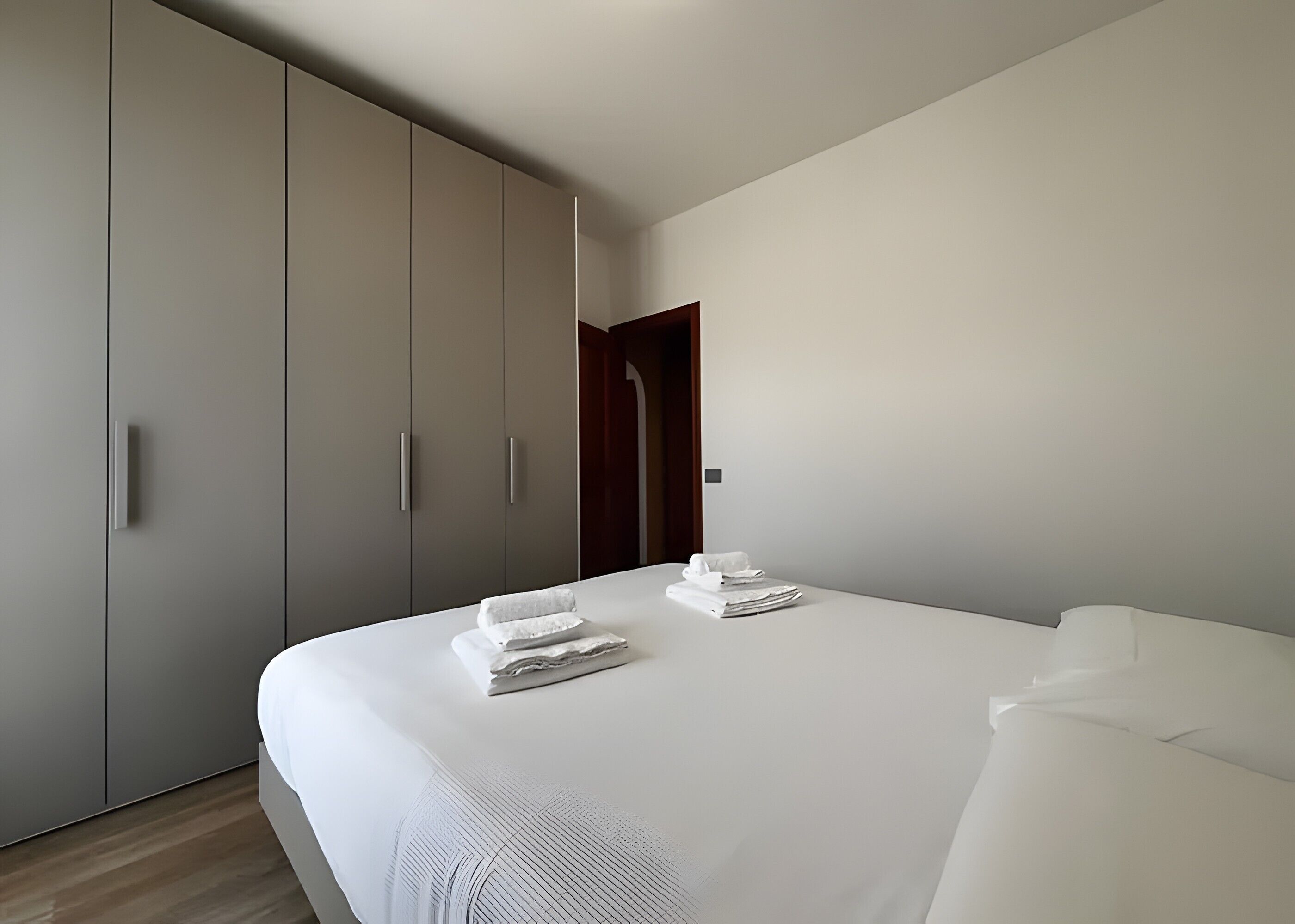 A modern hotel room with a large bed, a wardrobe, and a door leading to another room.
