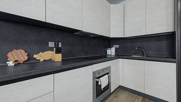 Cozinha moderna com bancada preta, eletrodomésticos de aço inoxidável e tábua de corte de madeira.