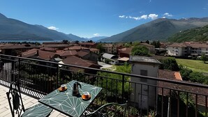 Eine Terrasse mit Tisch und Stühlen, die auf eine Stadt mit Gebäuden und Bergen in der Ferne blickt.