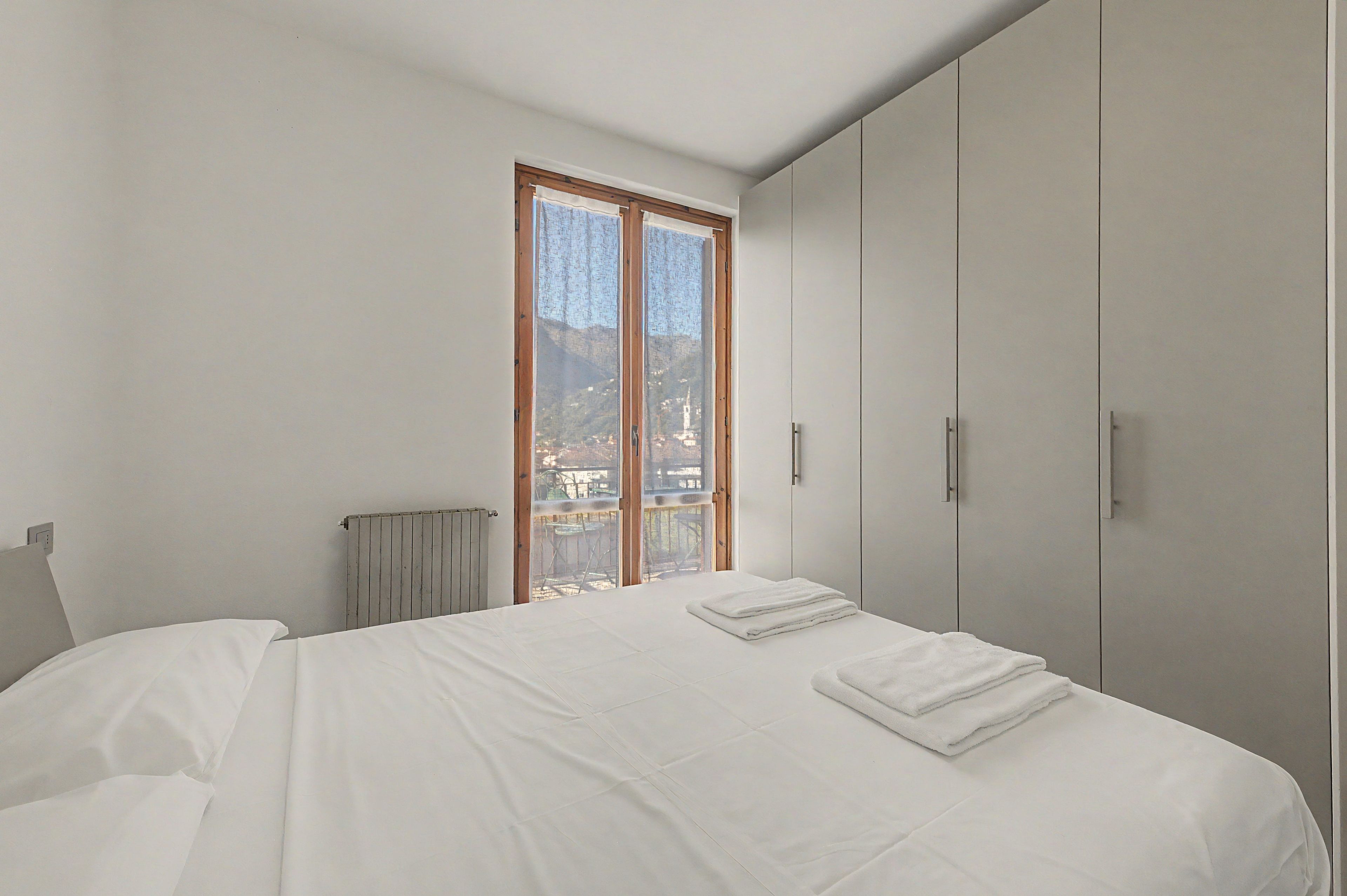 A bedroom with a large bed, a wardrobe, and a window with a view.