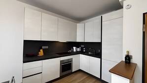 Eine moderne Küche mit weißen Schränken, einer schwarzen Arbeitsplatte und einer Weinflasche auf einem kleinen Tisch.