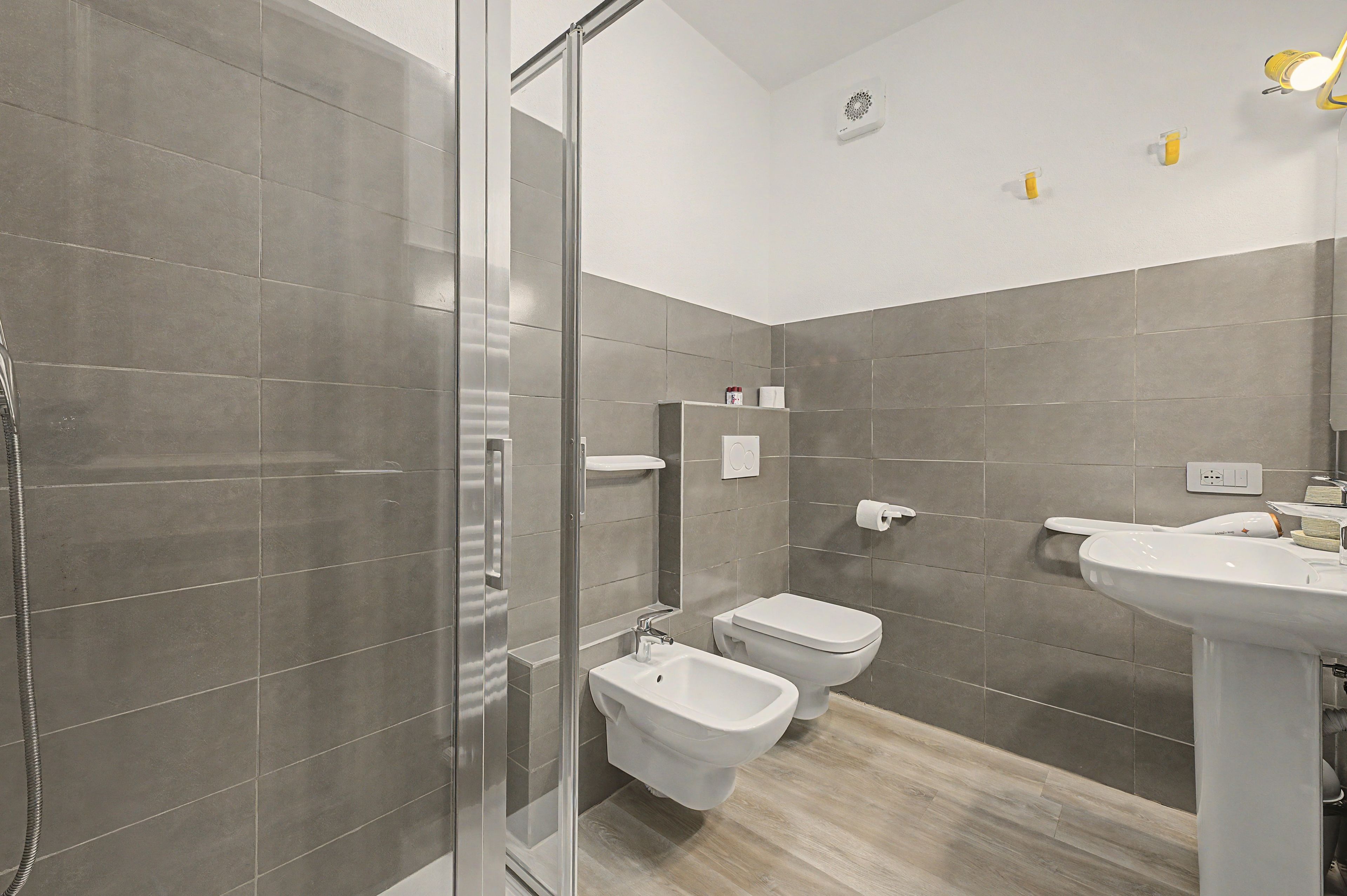 Un bagno moderno con cabina doccia in vetro, un bidet, un water e un lavabo.