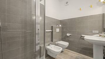 Un bagno moderno con cabina doccia in vetro, un bidet, un water e un lavabo.