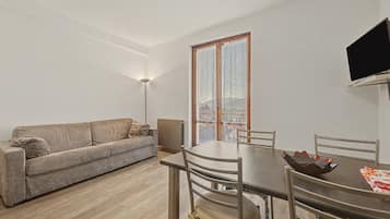 Een moderne woonkamer met een bank, een eettafel, stoelen en een aan de muur bevestigde televisie.