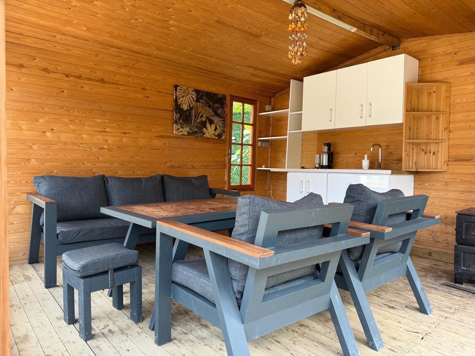 A cozy cabin interior with a wooden ceiling, a sofa set, a dining table, and a kitchenette.