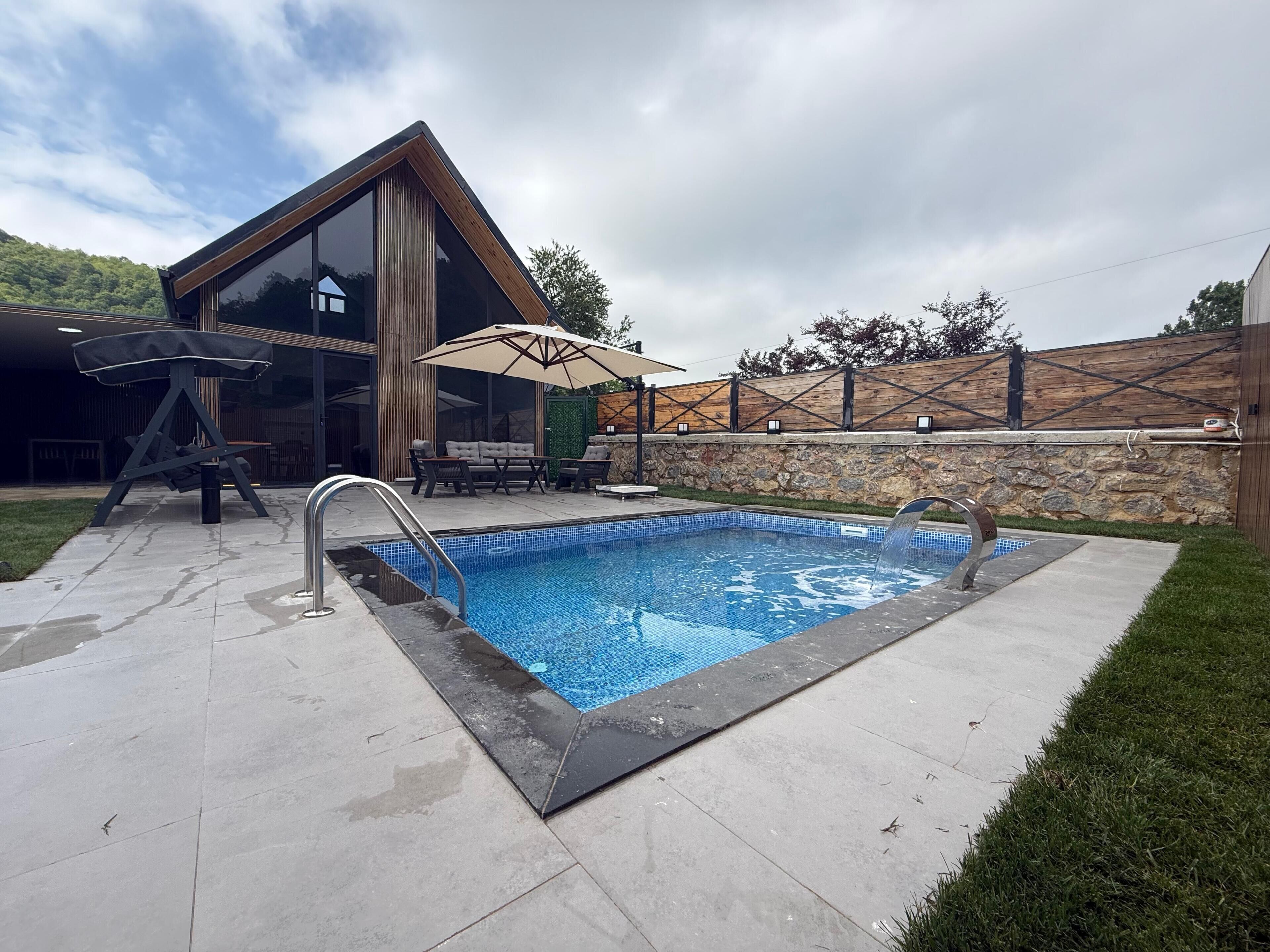 Zona de piscina exterior moderna amb un bany d'hidromassatge integrat, un solari de fusta i una paret de pedra.