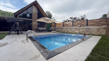 Zona de piscina exterior moderna amb un bany d'hidromassatge integrat, un solari de fusta i una paret de pedra.
