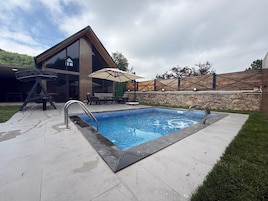 A modern outdoor pool area with a built-in hot tub, a wooden deck, and a stone wall.