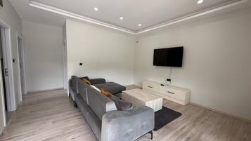 Una sala de estar moderna con un sofá seccional gris, una mesa de centro, un televisor de pantalla plana montado en la pared y un aparador blanco.