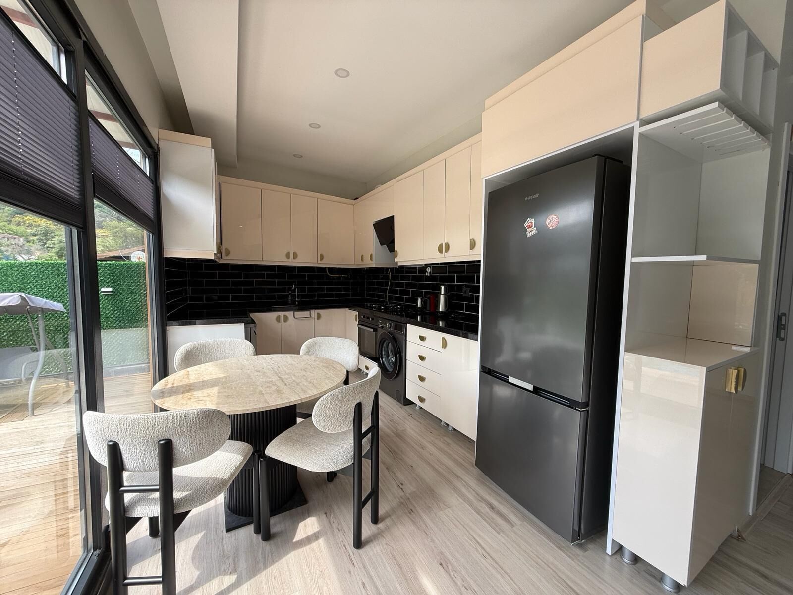 Una cocina moderna con un refrigerador negro, armarios blancos y una mesa redonda con sillas.