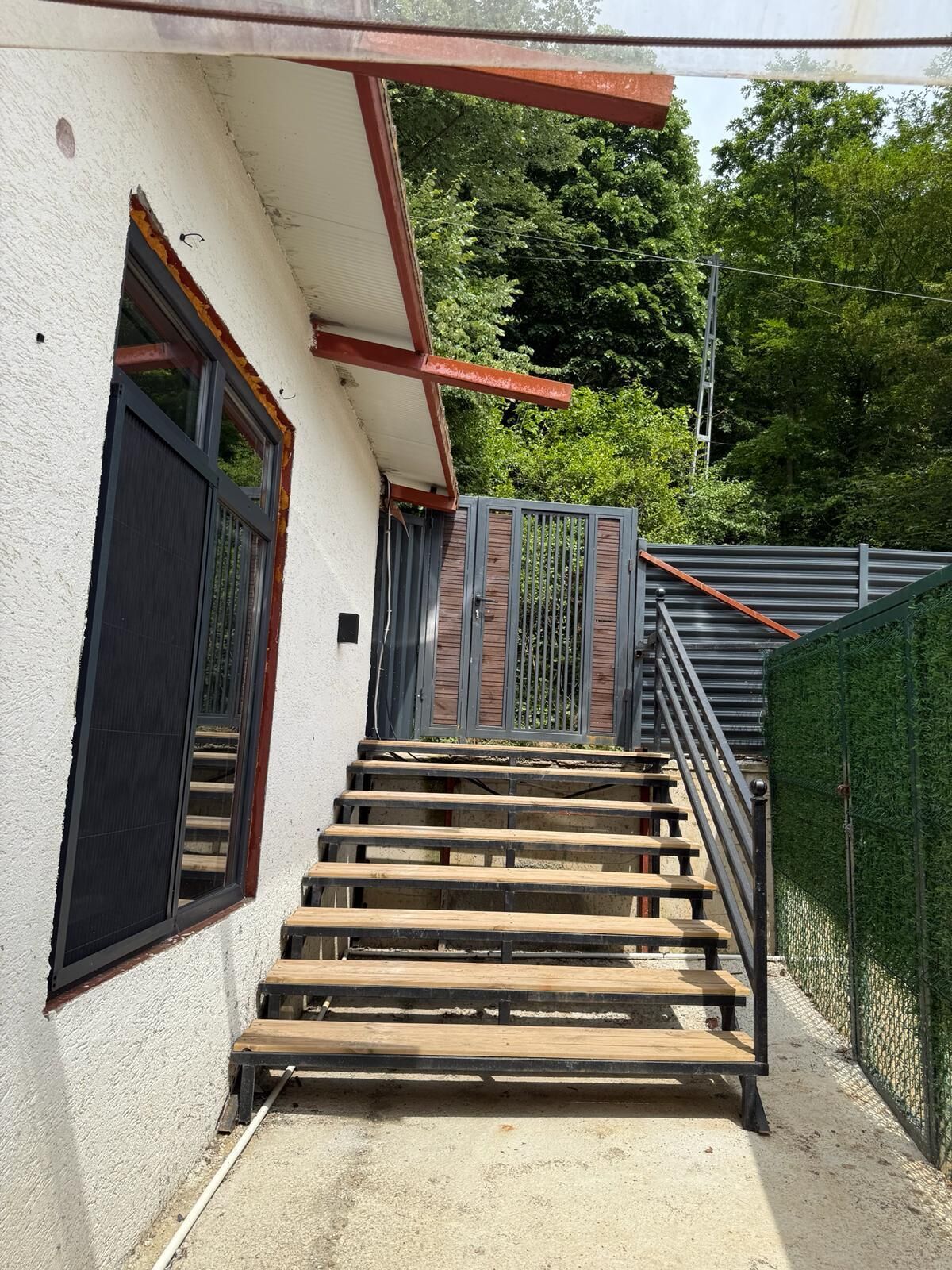 Una escalera que lleva a un edificio con una verja metálica y una cerca verde.