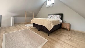 A bedroom with a sloped ceiling, a bed with a patterned headboard, a small window, and a wooden floor.