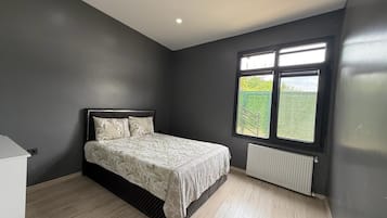 Un dormitorio con cama, un radiador y una ventana con vistas al verdor.