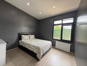 Un dormitorio con cama, un radiador y una ventana con vistas al verdor.