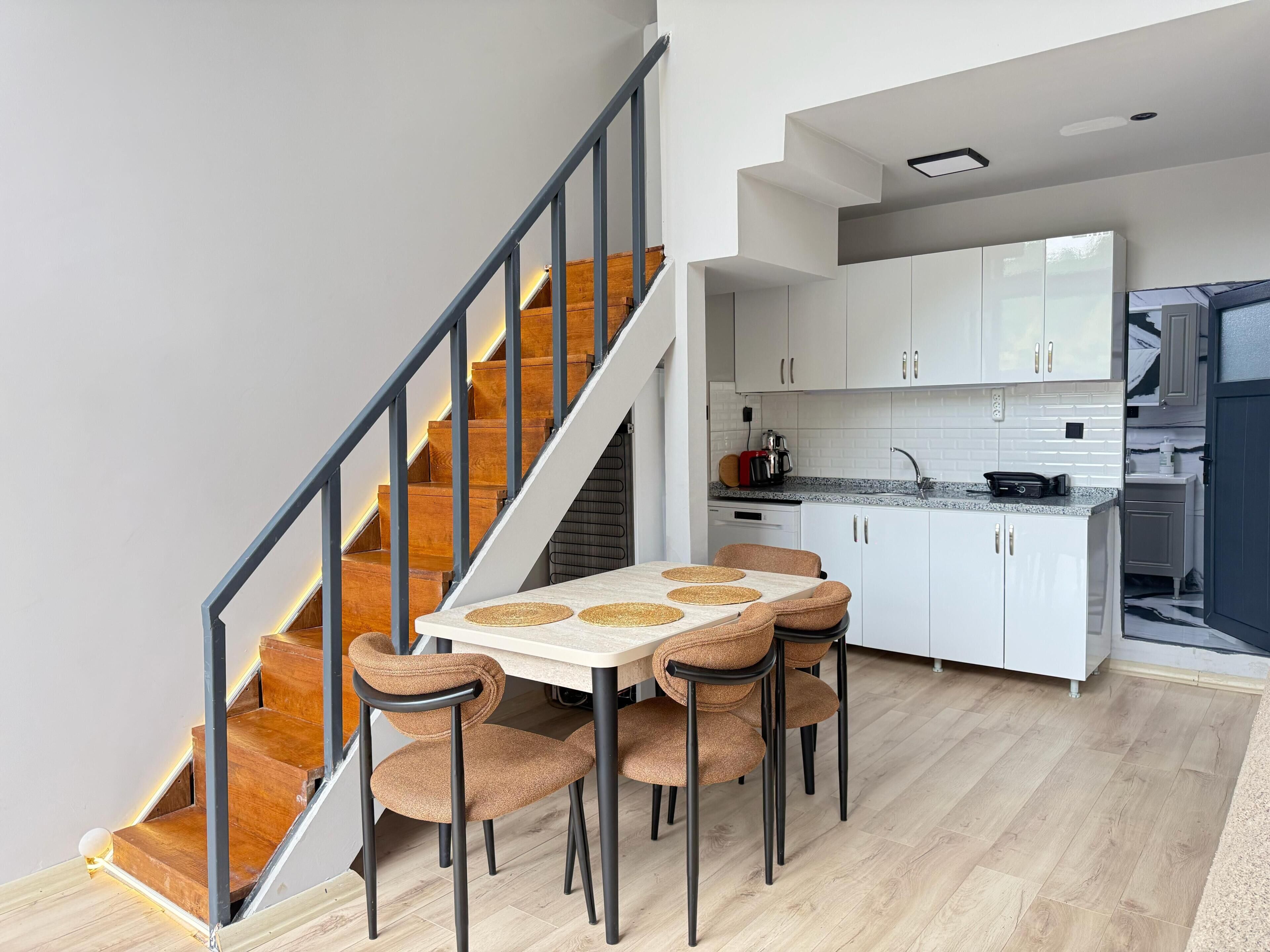 Una cocina moderna con armarios blancos, horno empotrado y comedor con mesa y sillas.