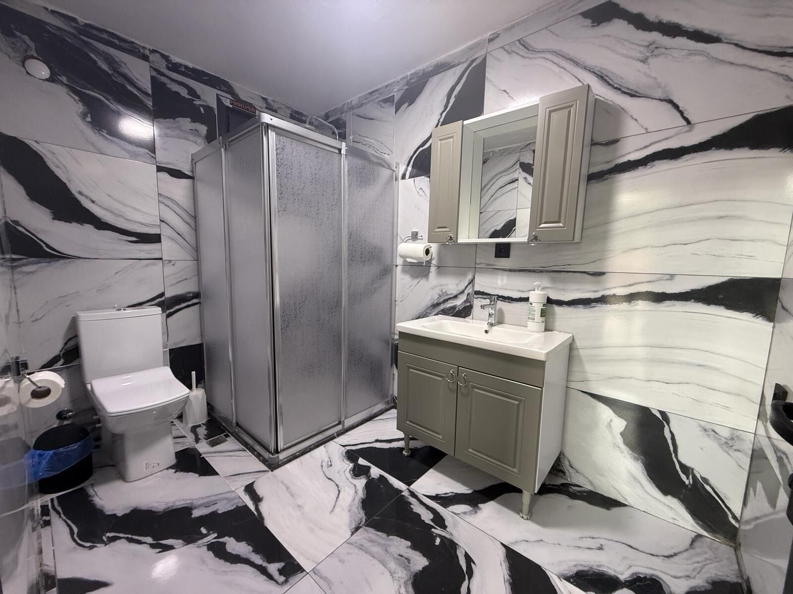 Un baño con inodoro, ducha, lavamanos y espejo.