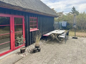 A building with a thatched roof, red-framed windows, and a patio area with a table and chairs.