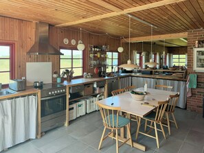 A kitchen with wooden cabinetry, a central island, and a dining area with chairs. - Thatched holiday home on the Limfjord's edge (Spoettrup)
